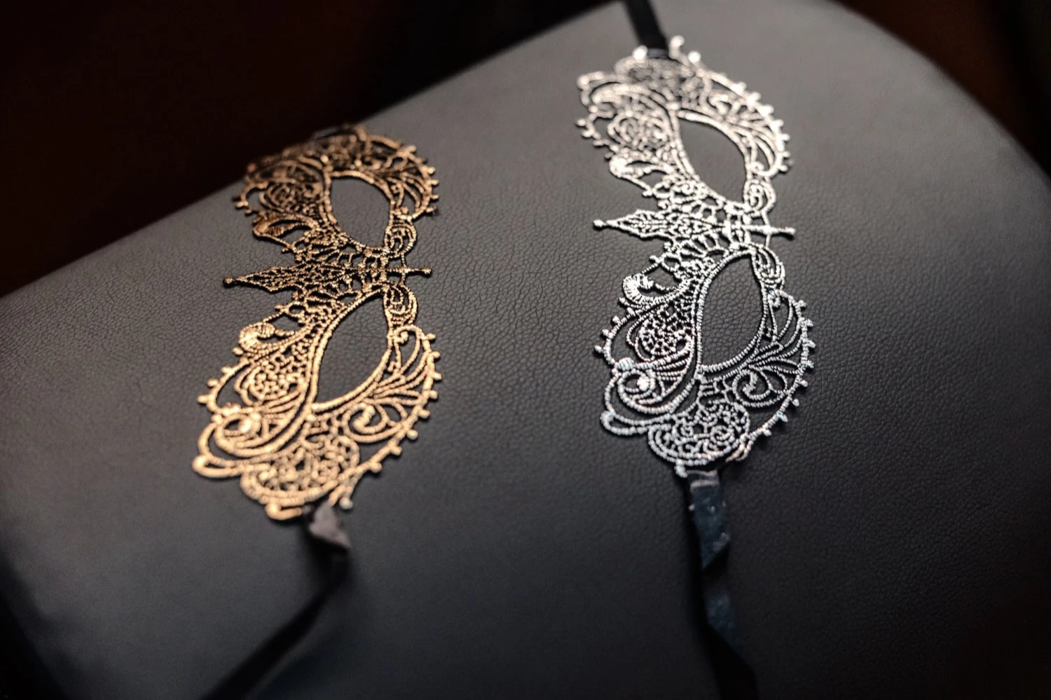 Deux masques de dentelle, or et argent, posés sur cuir sombre